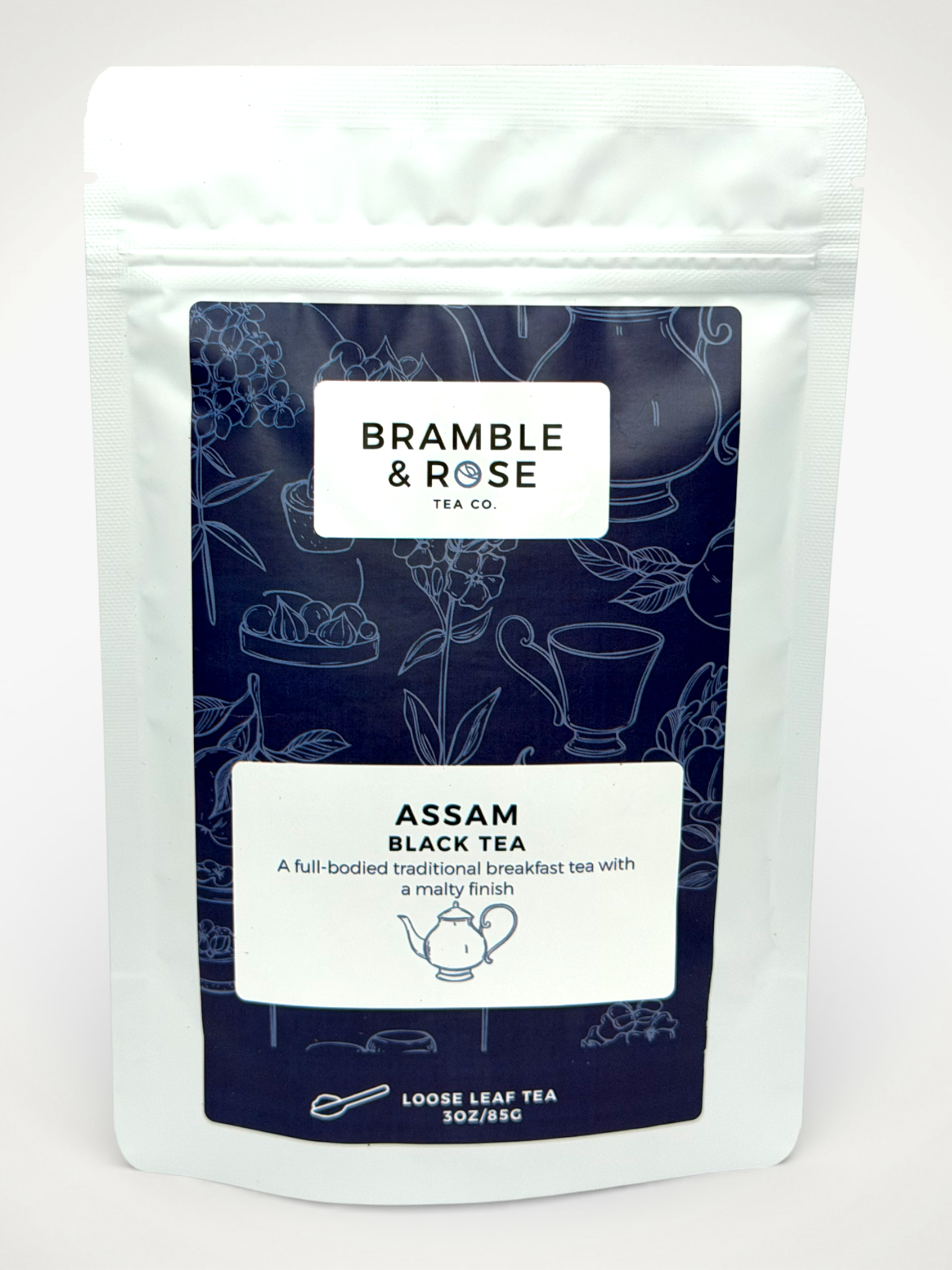 White pouch of Bramble & Rose Assam Black Tea, with a dark blue design featuring tea themed illustrations, a white rectangle with product description, and the "Bramble & Rose" logo.