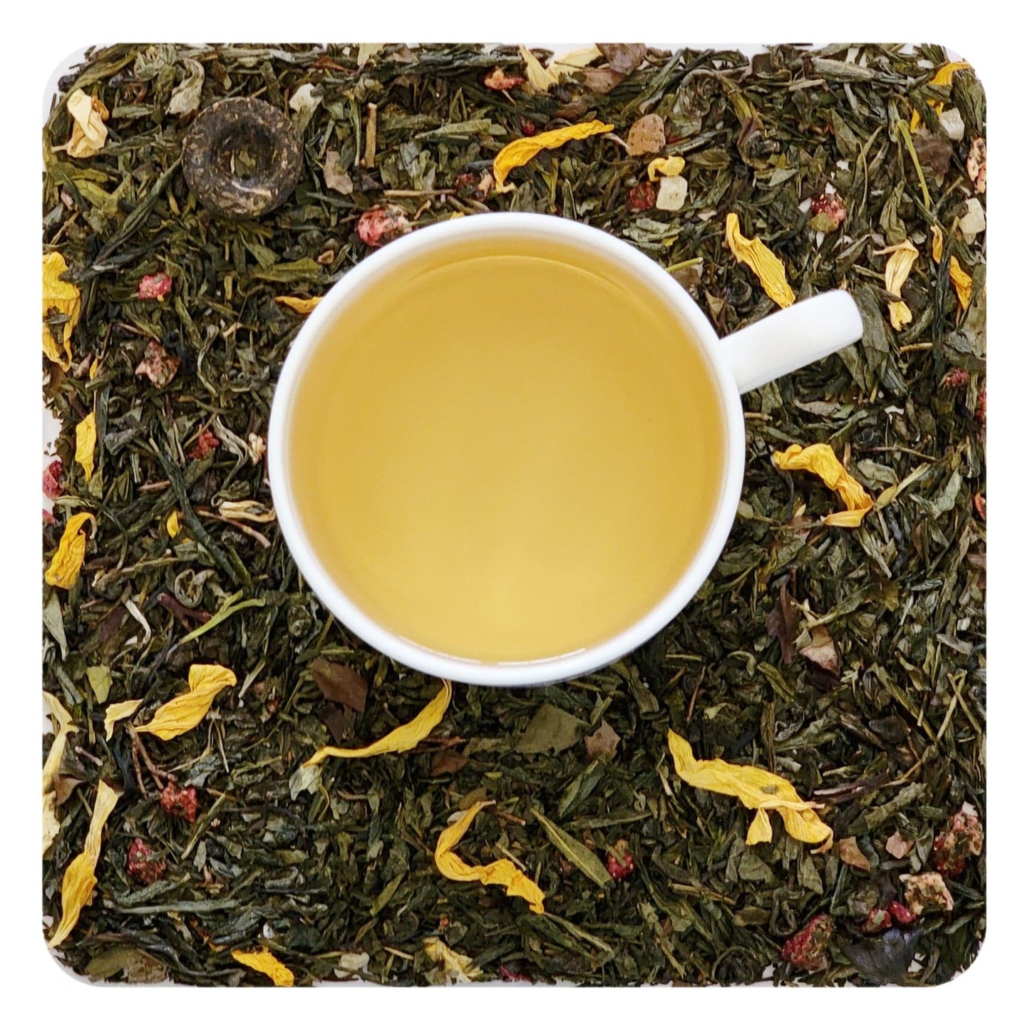 An overhead image of dried Bramble & Rose Tea Co. Aloha Berry Green tea  loose leaf tea including pieces of dried strawberry, pineapple, and flower petals. There is a white tea cup in the center with a pale yellow liquid of steeped Aloha Berry green tea