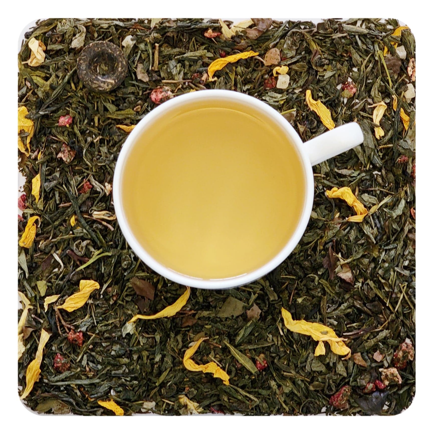 An overhead image of dried Bramble & Rose Tea Co. Aloha Berry Green tea  loose leaf tea including pieces of dried strawberry, pineapple, and flower petals. There is a white tea cup in the center with a pale yellow liquid of steeped Aloha Berry green tea