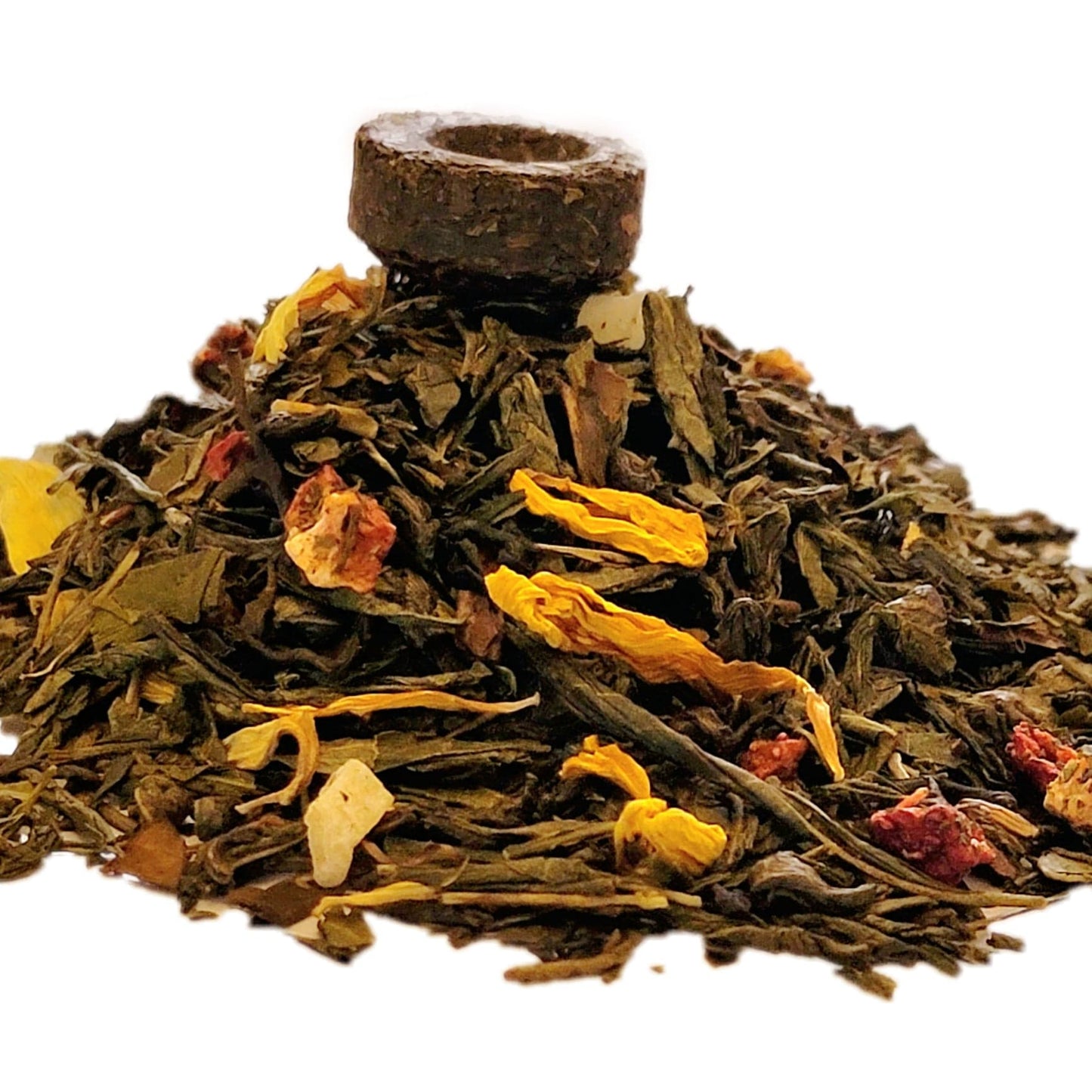 A close-up image of dried Aloha Berry Green tea leaves including dried pieces of strawberry, pineapple, and flower petals with a compressed mini-tuo tea cake on top.