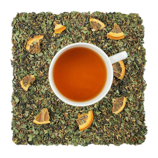 An overhead image of dried Bramble & Rose Tea Co. Breathe Green tea  loose leaf tea including pieces of dried citrus fruits. There is a white tea cup in the center with a light brown/gold liquid of steeped ActiviTea green tea