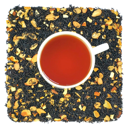 An overhead image of dried Bramble & Rose Tea Co. Butter Cookie Bliss Black loose leaf tea including pieces of dried citrus peel and almonds. There is a white tea cup in the center with a light brown liquid of steeped Butter Cookie Bliss Black tea