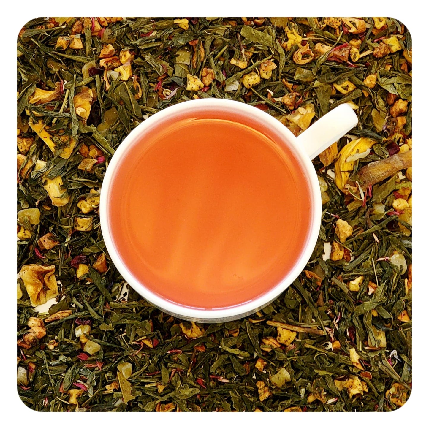 A cup of tea, showcasing a bright orange infusion, surrounded by a bed of dried green tea, mango, guava, and other herbs, representing the ingredients of the tea blend.