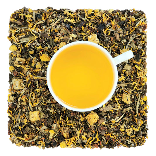 A cup of peach tea on a bed of dried white tea leaves, pieces of fruit and floral petals, and other dried herbs  indicating the ingredients of the tea blend.