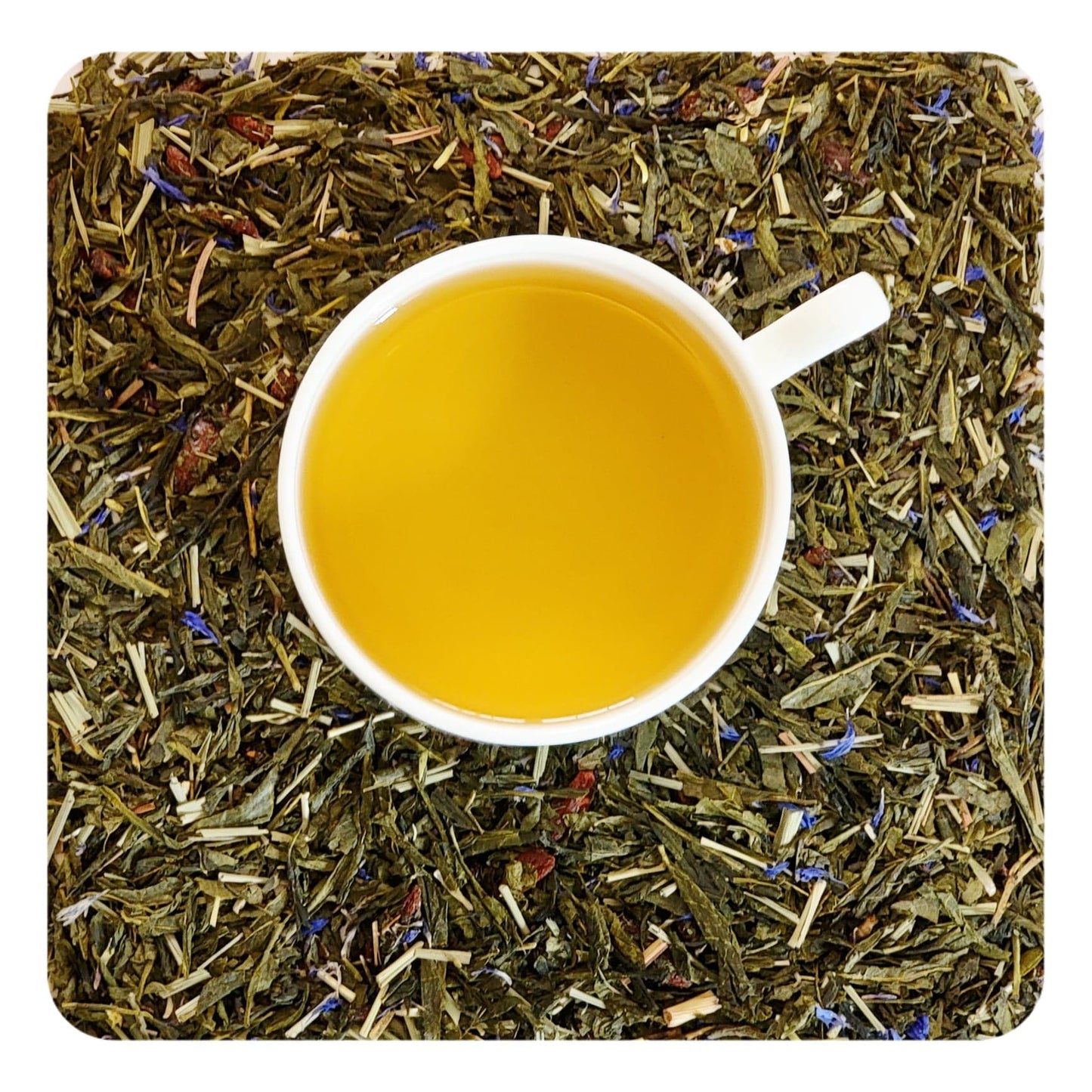 A cup of pomegranate green tea served on a bed of dried green tea leaves with visible pieces of fruit and flower petals, indicating the ingredients of the tea blend.