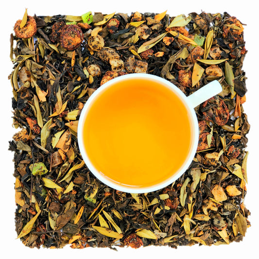 A cup of strawberry kiwi quencher brewed tea on a bed of loose white tea leaves with dried pieces of strawberry, pineapple, and kiwi. 